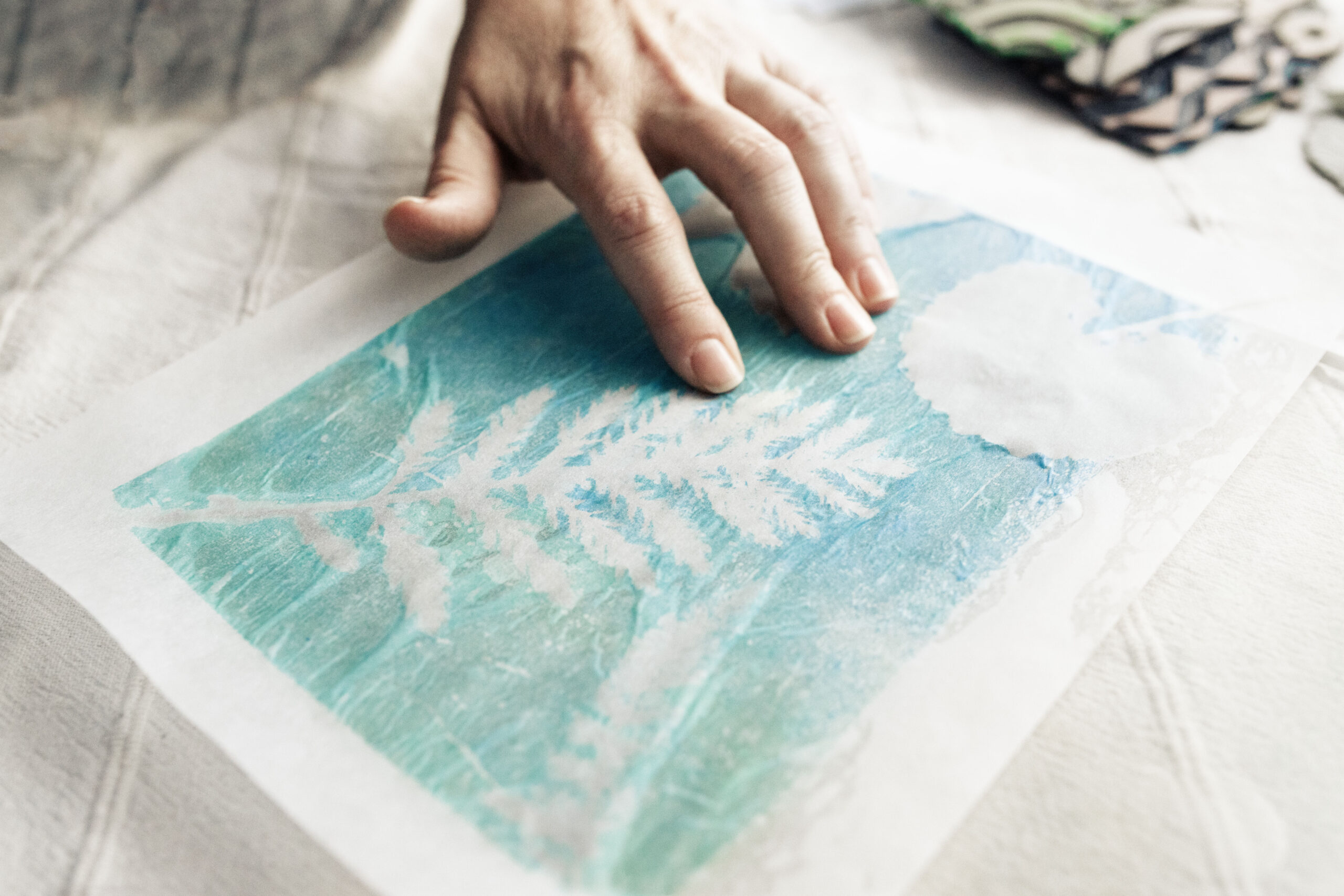 A hand of the founder and designer of Inner Imprints Arts Studio touching a turquoise botanical gelli print on paper.