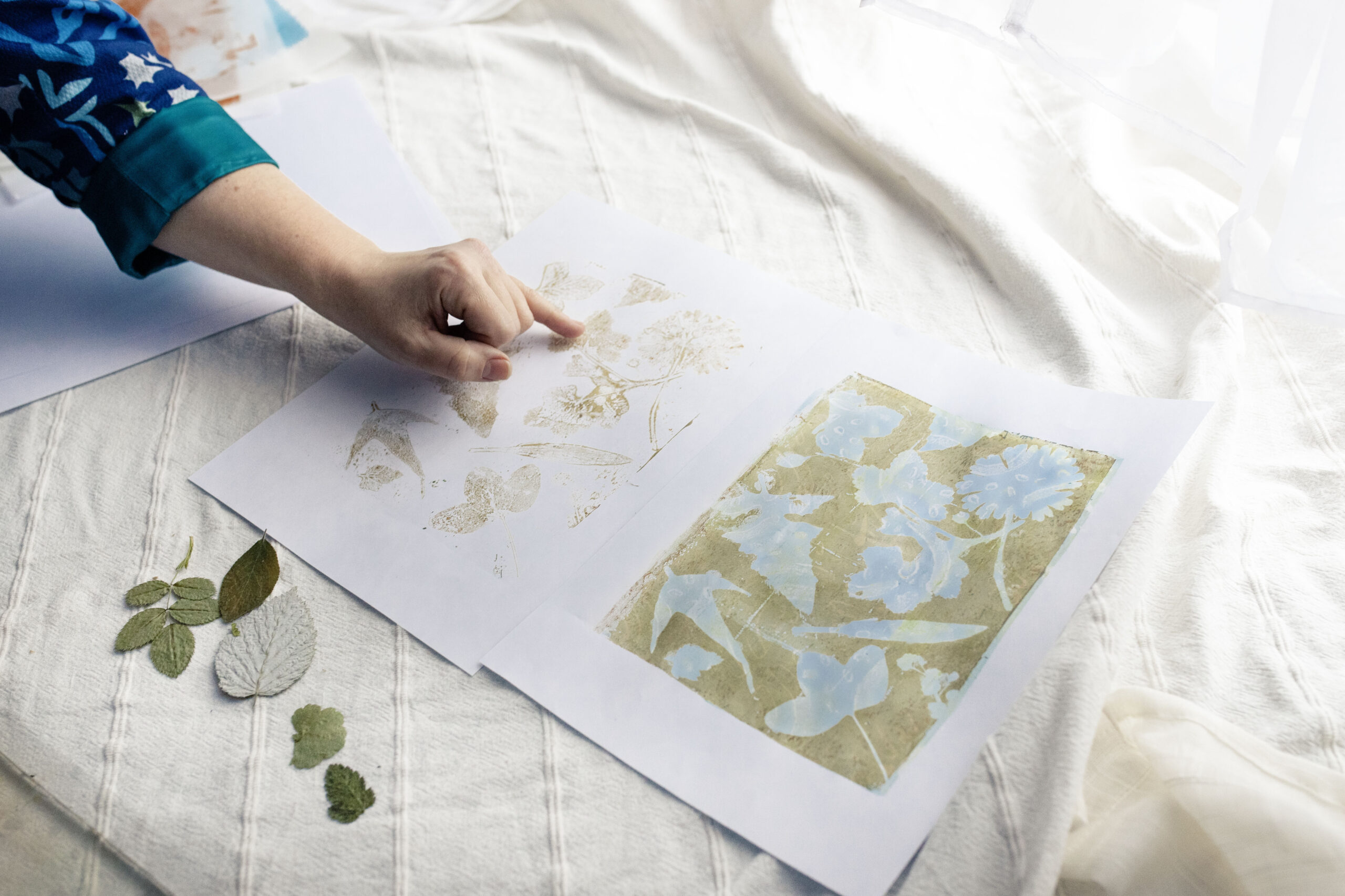 A hand of the founder and designer of Inner Imprints Arts Studio pointing to two botanical prints laid side by side on paper that represent the interplay between figure and ground.