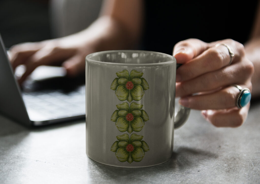 A close-up of a light grey mug decorated with three vertically aligned green flowers featuring red and orange centers, artwork by Inner Imprints.