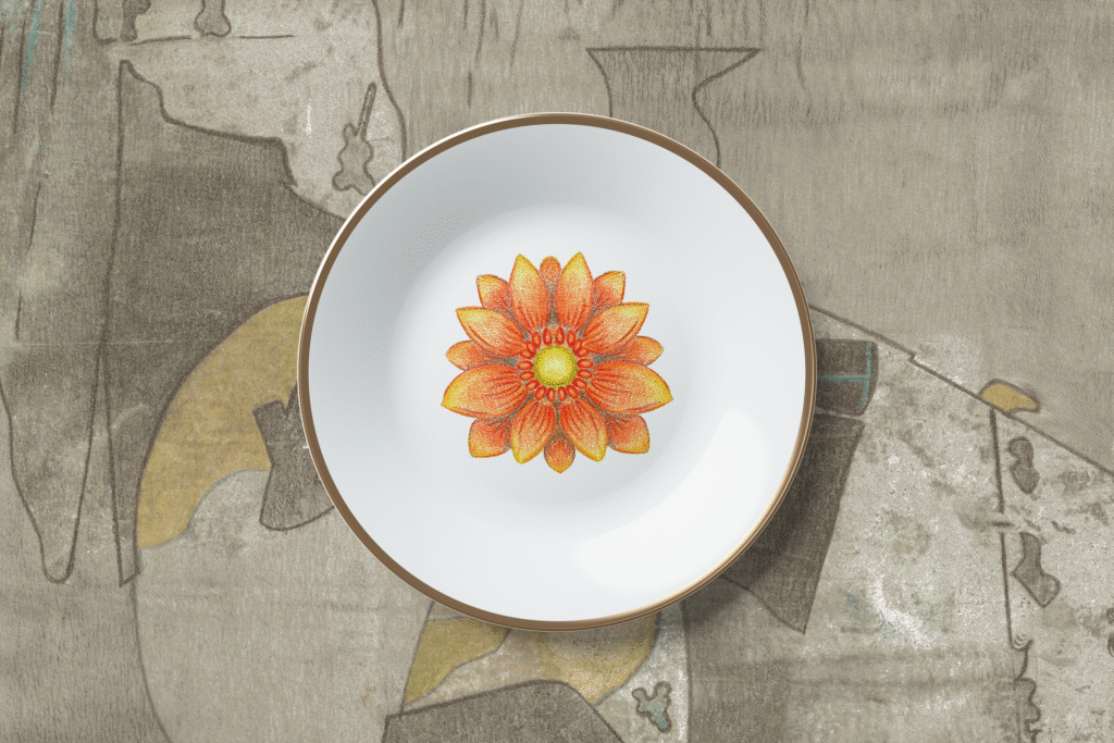 Mockup showing a ceramic plate with a hand-drawn, coloured flower placed on a patterned place mat. Both the floral motif and the background print are original artworks, combining hand drawing, colouring, and textile-inspired surface pattern design.